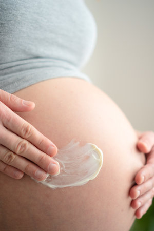Serene expecting mother carefully applying anti-stretch mark cream. Loving self-care ritual to nurture changing pregnant body at home.の写真素材
