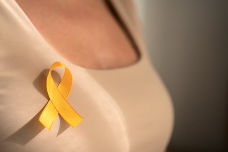 Detailed focus on yellow awareness ribbon pinned to females shirt, symbolizing support for pediatric cancer patients and their families.の写真素材