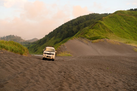 4x4 adventure car parked on secluded sandy beach between green mountains and ocean waves. Perfect...