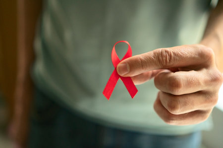 Mans hand carefully holding red satin ribbon symbolizing HIV AIDS awareness support for affected...