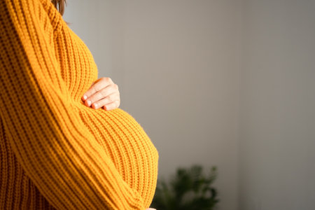 Close-up of expecting mother gently stroking her rounded belly in peaceful home setting. Tender...