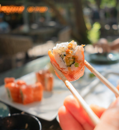 Fresh salmon and cucumber sushi roll held with chopsticks, beautifully presented with authentic...