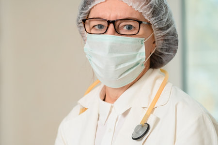Close-up of senior female doctor in white coat and medical mask. Stethoscope around her neck, she...
