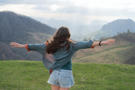 Adventurous female standing with open arms before majestic mountain range. Wind blows through her...