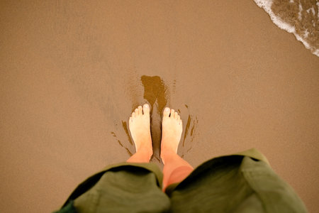 Top down photography of female feet enjoying ocean waves and foam on perfect sandy beach. Summer...
