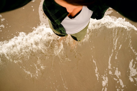 Top down view of female feet touching ocean waves on sandy beach.の写真素材