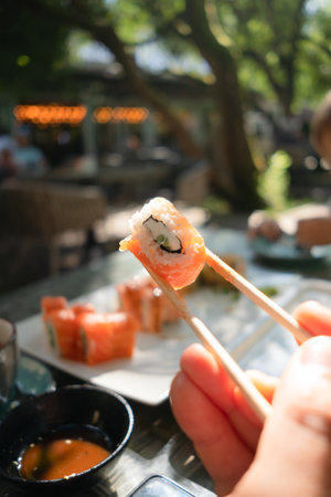 Appetizing sushi roll filled with fresh salmon and crisp cucumber, captured mid-air with chopsticks against restaurant backdrop.の写真素材