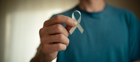 Close up of a young man holding a blue satin ribbon. Concept of prostate cancer awareness in November, medical diagnosis, treatment, and support from family and community.の写真素材