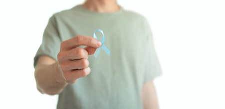 Close up of a young man holding a blue ribbon in his hand isolated over white. Symbol of prostate cancer awareness, early diagnosis, medical support, oncology care, and prevention concept.の写真素材