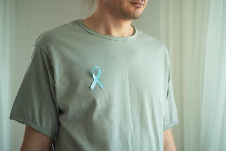 Close up of a young man wearing a blue ribbon on his shirt. Symbol of prostate cancer awareness month, early diagnosis, medical help, and support from family and loved ones.の写真素材