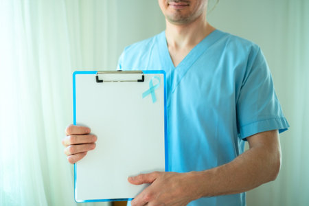 Close up of young man healthcare worker with blue satin ribbon and empty clipboard sheet. November prostate cancer awareness, prevention, and medical diagnostics concept.の写真素材
