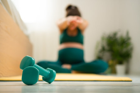 Close-up of dumbbells, pregnant woman training in the background. Light workout during pregnancy.の写真素材