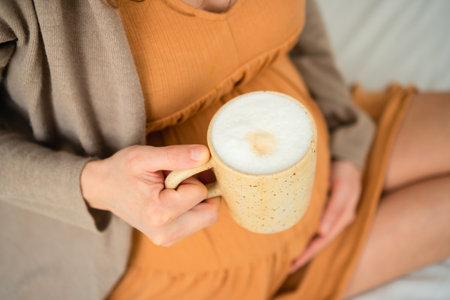 Mom-to-be savoring warm coffee drink in peaceful home setting. Responsible caffeine intake discussion during gestation period.の写真素材