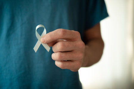 Close up of a man holding a blue ribbon in his hand. Symbol of prostate cancer awareness in...