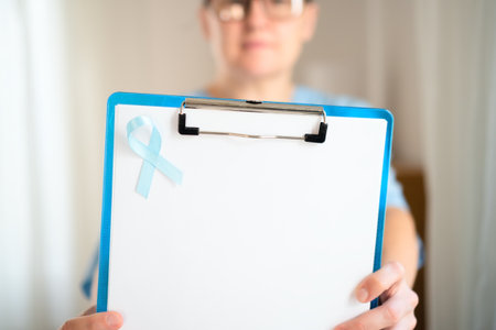 Close up of nurse in medical clothing with blue ribbon on uniform and clipboard in hands. November awareness month for prostate cancer and early health diagnosis prevention.の写真素材