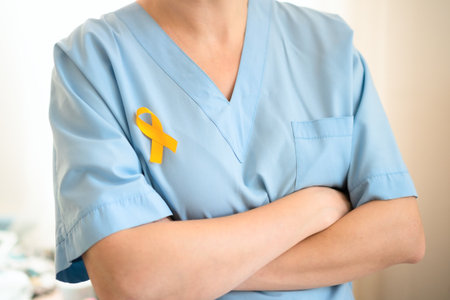Female medical staff in uniform with yellow ribbon pinned on clothing. Symbol of childhood cancer awareness, medical help, diagnosis, timely treatment, family support, and healthcare vigilance.の写真素材