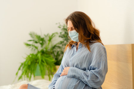 Mom-to-be wearing safety mask while recovering in bed. Important infection control measures during sensitive pregnancy period.の写真素材