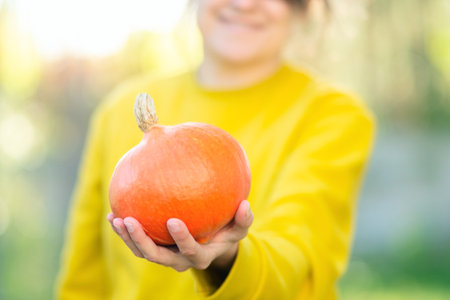 Smiling female farmer holding a ripe pumpkin in her hands on the farm during harvest season. Organic vegetables, healthy food, natural nutrition, and autumn freshness.の写真素材
