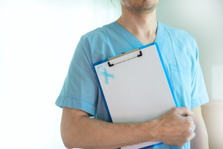Doctor or medical staff man in uniform holding clipboard with blue ribbon and blank paper. Symbol of prostate cancer awareness, health prevention, and early diagnosis in November.の写真素材