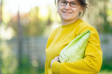 Young female farmer holding spire cabbage from her farm. Seasonal vegetables, fresh harvest, healthy eating, fiber, and pride in homegrown produce. Unique cabbage variety.の写真素材