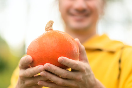Close up of pumpkin in male hands, smiling farmer behind. Autumn harvest, organic food, countryside lifestyle, natural produce, and proud rural farming.の写真素材
