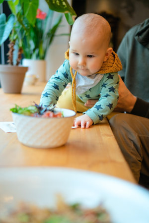 Father with toddler reaching for food. Parenting, care, family values and love. Happy moment of connection and curiosity during meal in public place.の写真素材