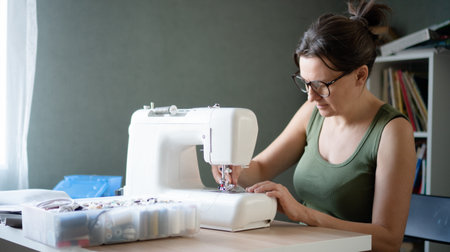 Female tailor using a professional sewing machine to create and assemble a new garment in her bright...