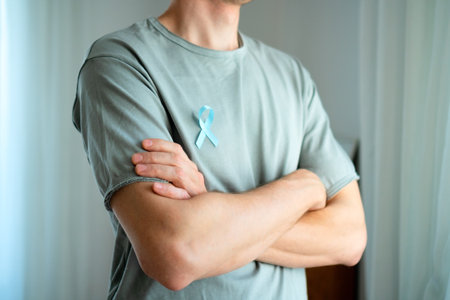 Man standing with crossed arms wearing blue satin ribbon on shirt. Concept of prostate cancer awareness in November, prevention, early diagnosis, and medical care for mens health.の写真素材