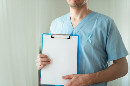 Close up of young man healthcare worker with blue satin ribbon and empty clipboard sheet. Horizontal Banner for November prostate cancer awareness, prevention, and medical diagnostics concept.の写真素材