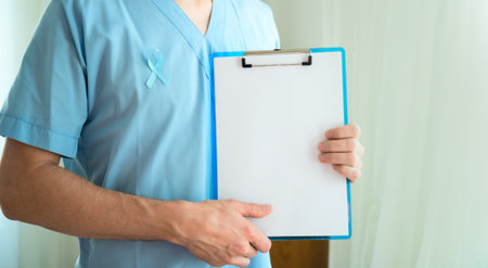 Male healthcare professional in uniform with blue ribbon symbol of prostate cancer awareness holding clipboard with empty paper for notes and reminders in November. Horizontal Bannerの写真素材