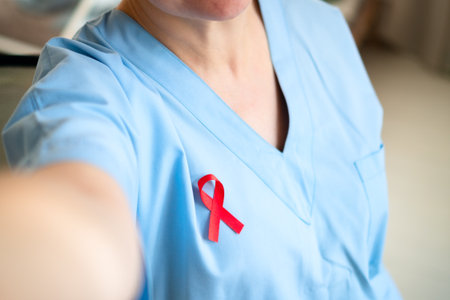 Woman medical professional taking phone selfie with red ribbon on uniform, showing support and...