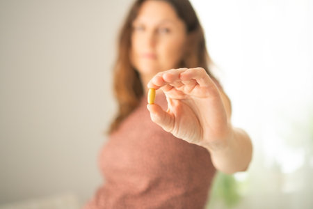 Pregnant female carefully examining pill before intake while touching her bump. Thoughtful health management during gestation period.の写真素材