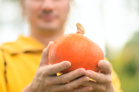 Close up of pumpkin in male hands with smiling farmer in background. Autumn harvest, organic farming, pride for own crop, healthy vegetable, natural lifestyle, and nutrition.の写真素材