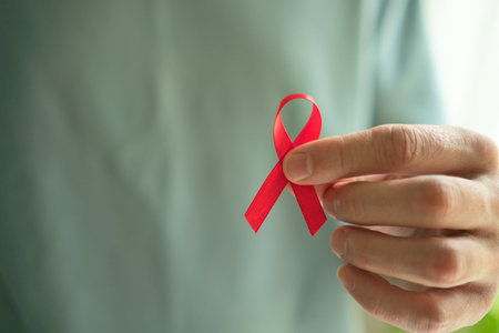 Mans hand carefully holding red satin ribbon symbolizing HIV AIDS awareness support for affected people and December hope.の写真素材