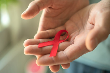 Close-up of male hands offering red awareness ribbon on palm, representing December HIV AIDS...