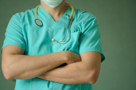 Portrait of a professional male doctor in medical mask and stethoscope, arms crossed on chest....