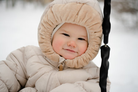 An adorable toddler, dressed in a warm snowsuit, enjoying a winter swing. The cozy outfit and curious expression highlight the joy of outdoor play for a baby, child, or newborn in snowy weather.の写真素材
