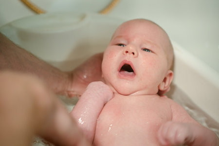 A newborn expresses surprise and curiosity during bath time, supported by a loving parent hand, highlighting the emotional connection and discovery in early life.の写真素材