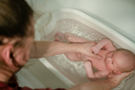 A tender moment of a newborn bath, supported by a parents hand, emphasizing safety, gentleness, and the loving care that defines early parenting experiences.の写真素材