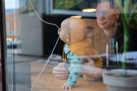 Man with baby in cafe, father supporting child while seen through glass. Family values, love, parenting, bonding and warmth in public place with everyday happiness.の写真素材