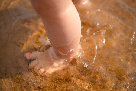 Baby feet splash in the shallow water, capturing the essence of freedom and fun on a sunny beach day, highlighting the simple pleasures and exploration of early childhood.の写真素材