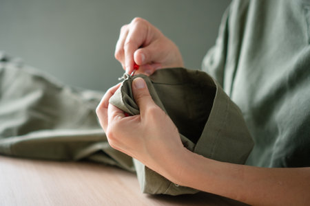 Woman dressmaker in her studio removing the lower seam from a pair of trousers for repair or...