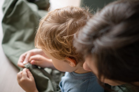 Busy mother working as a tailor at home, unpicking a seam on trousers with her baby sitting on her...