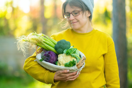 Close up of smiling girl farmer holding basket with broccoli, cauliflower, kohlrabi and young corn....