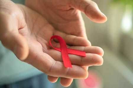 Close-up of male hands opening to reveal red satin ribbon on palm, symbolizing HIV AIDS support,...