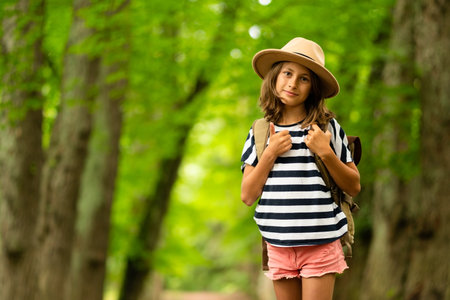 Radiant girl with hiking gear smiles brightly at camera, standing on forest path. Embodiment of youthful summer adventure spirit.の写真素材