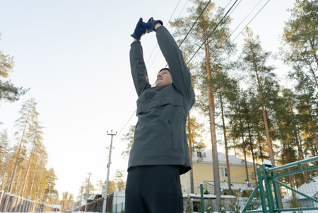 A guy in his forties pulls his arms up during an outdoor warmup. Man prepares for a run in cold...
