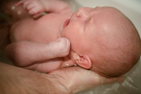 A tender moment of a newborn bath, supported by a parents hand, emphasizing safety, gentleness, and...