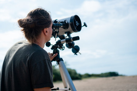 close-up from behind man intently observing through a telescope on the beach. shot focuses on his...