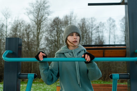 Extreme closeup of a focused young woman holding a metal bar while exercising on outdoor leg...